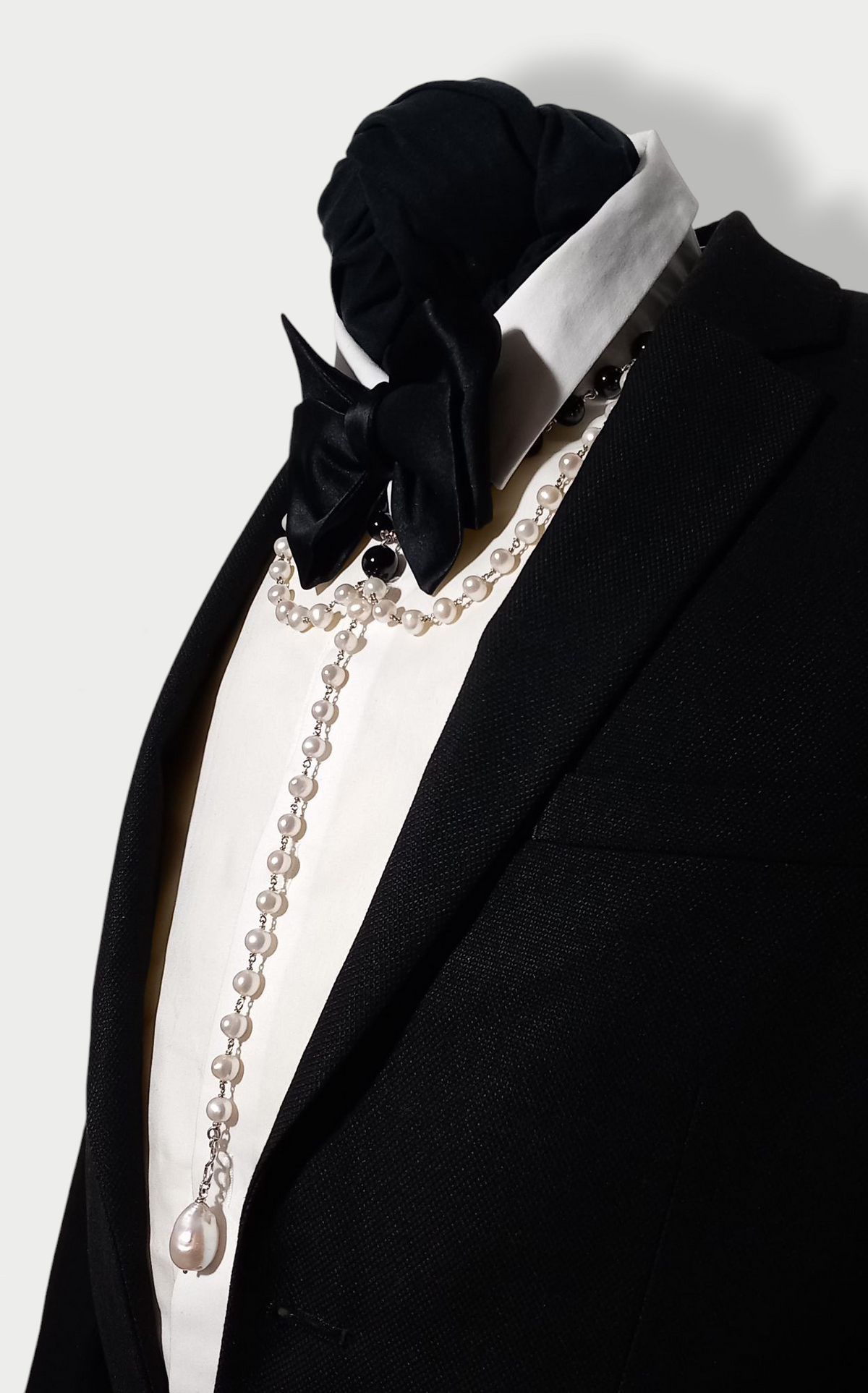A black and white composition necklace with pearls and onyx beads, silver (925) detailing, styled on a tuxedo under a bow tie to give a modern collar impression