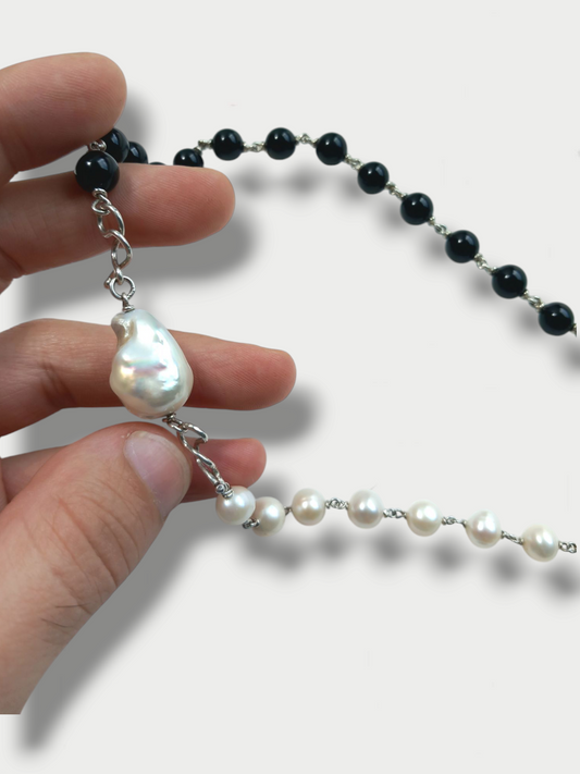 Detail of a two-tone necklace with a combination of pearls and onyx beads, featuring a central baroque pearl, on a white background.