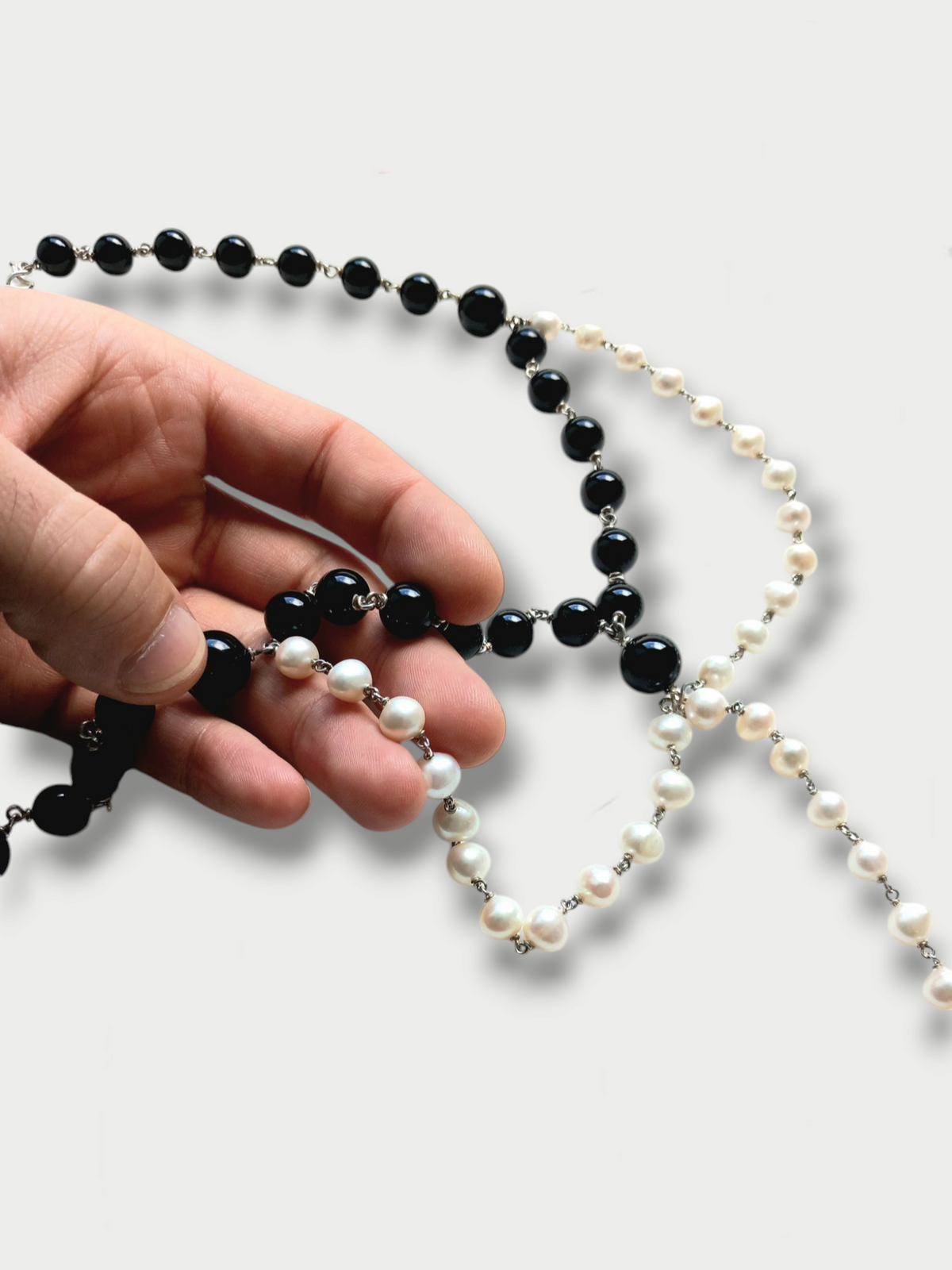 Hand held detail of a black and white composition necklace with pearls and onyx beads, silver (925) detailing, displayed against a white background.