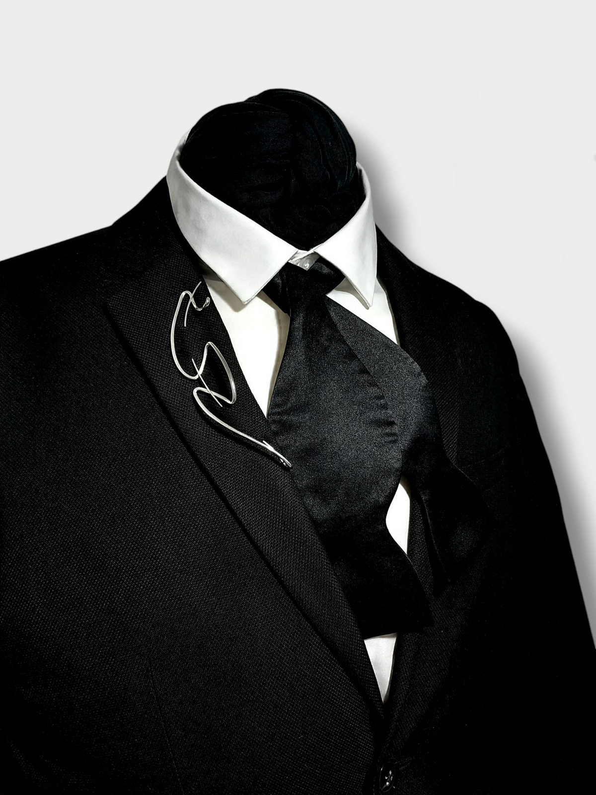 Simple silver(925) fluid experimental brooche worn on a black blazer lapel styled with an open bow tie 