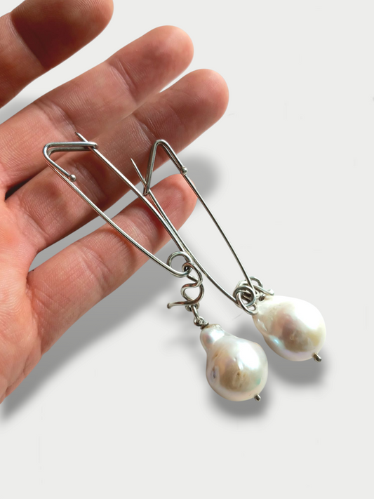 Pair of safety pin inspired cufflinks with baroque pearls drop hand held against white background